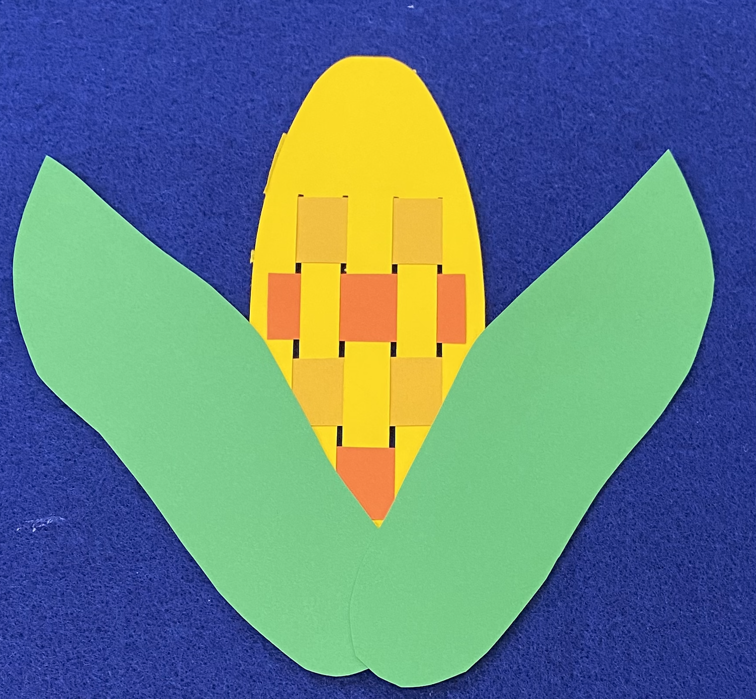 An ear of corn made out of yellow, gold, orange, and green paper on a blue background
