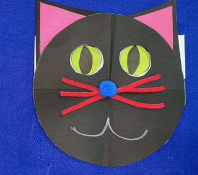 A paper black  at with green eyes, a blue nose, and pink whiskers on a dark blue background